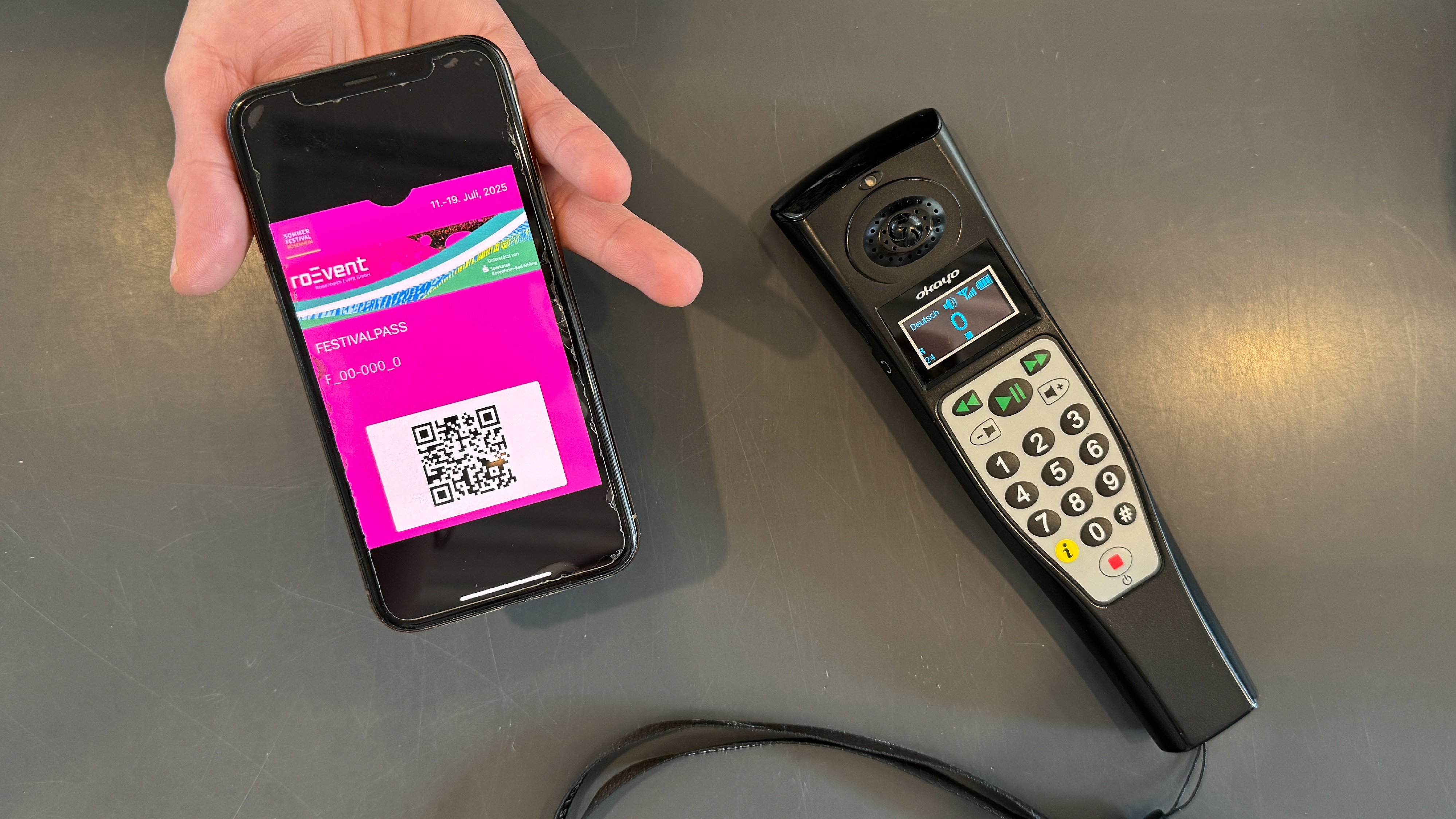 Hand mit Smartphone zeigt Sommerfestivalpass, daneben liegt ein Audioguide-Gerät für die Titanic-Ausstellung.