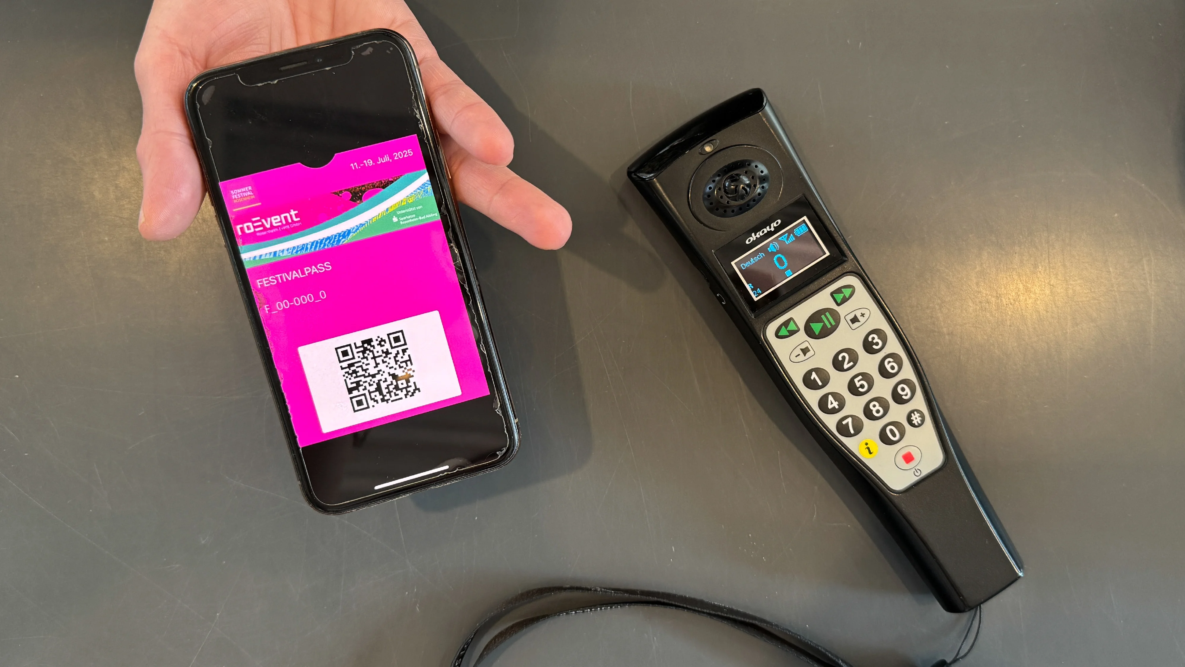 Hand mit Smartphone zeigt Sommerfestivalpass, daneben liegt ein Audioguide-Gerät für die Titanic-Ausstellung.