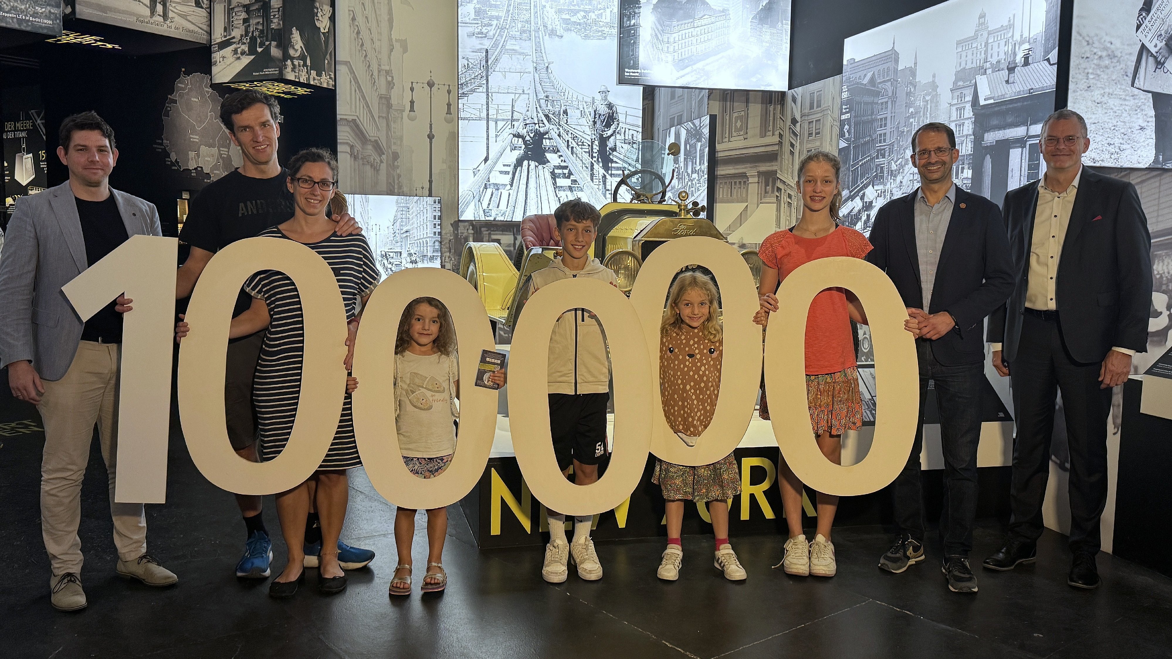 Jubiläumsbesucher-Familie mit großen Zahlen „100.000“ in der Titanic-Ausstellung im Lokschuppen Rosenheim.