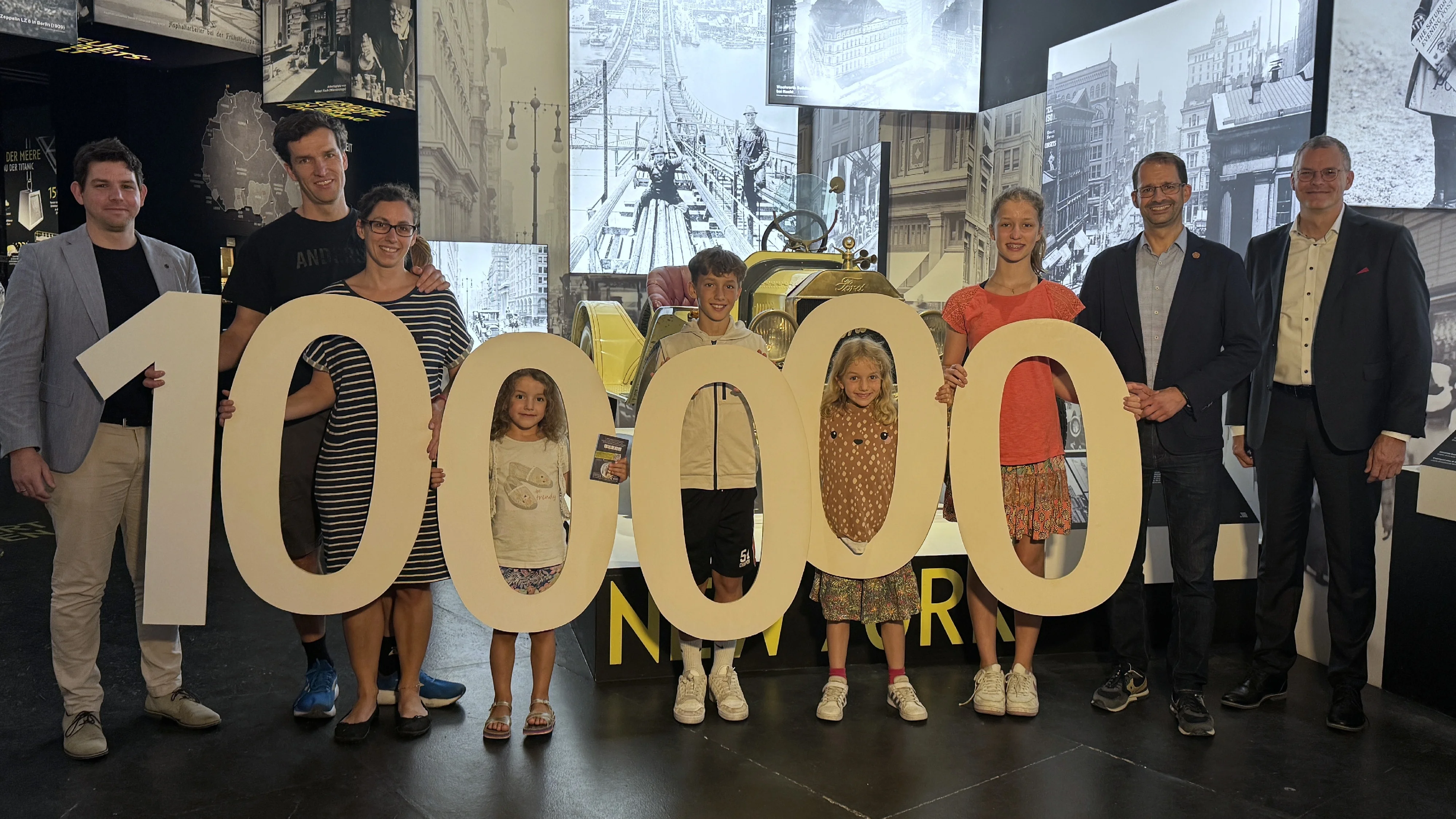 Jubiläumsbesucher-Familie mit großen Zahlen „100.000“ in der Titanic-Ausstellung im Lokschuppen Rosenheim.