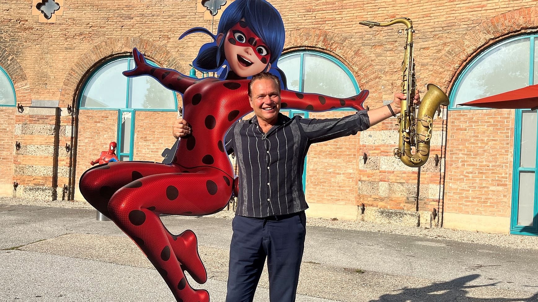 Saxophonist Mulo Francel von Quadro Nuevo posiert neben einer lebensgroßen Ladybug-Figur im Innenhof des Lokschuppens Rosenheim.
